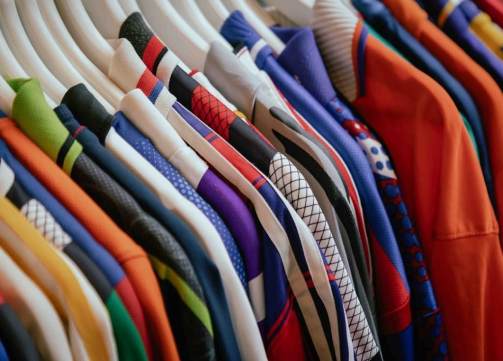 A close-up view of a rack of colorful clothing, featuring a variety of patterns and fabrics. The neatly arranged garments on white hangers display a mix of vibrant colors and designs, creating a visually striking retail display.