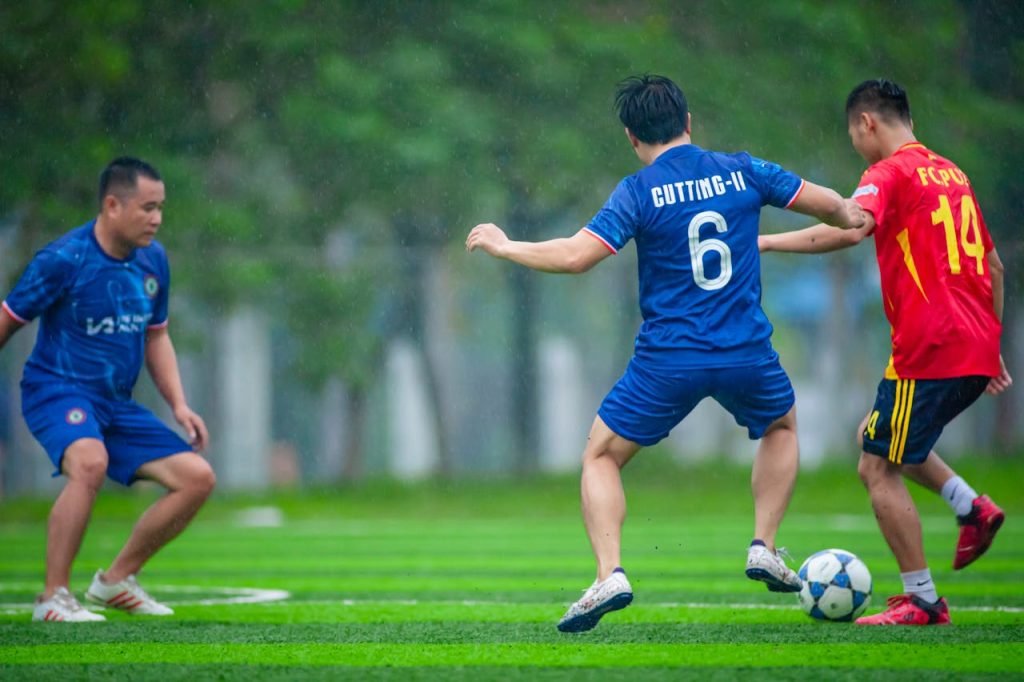 Three men playing football on a rainy day in Hanoi, Vietnam, showcasing skill and competition.