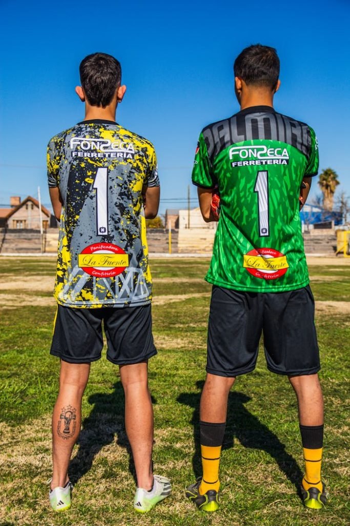 Two soccer players standing on a grassy field wearing team jerseys.